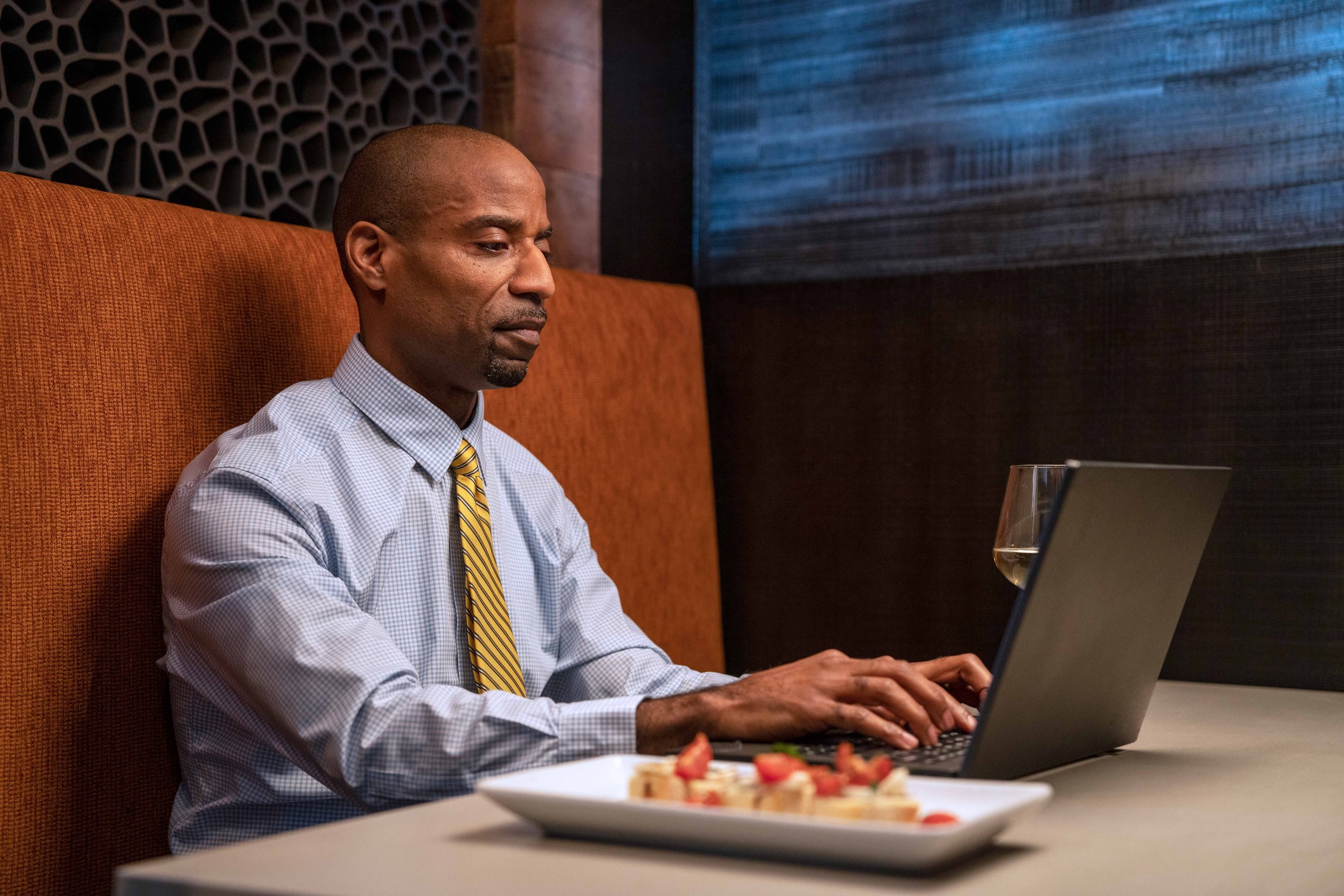 Vanderbilt student wearing a gold striped tie types on his laptop while having a meal in a restaurant booth