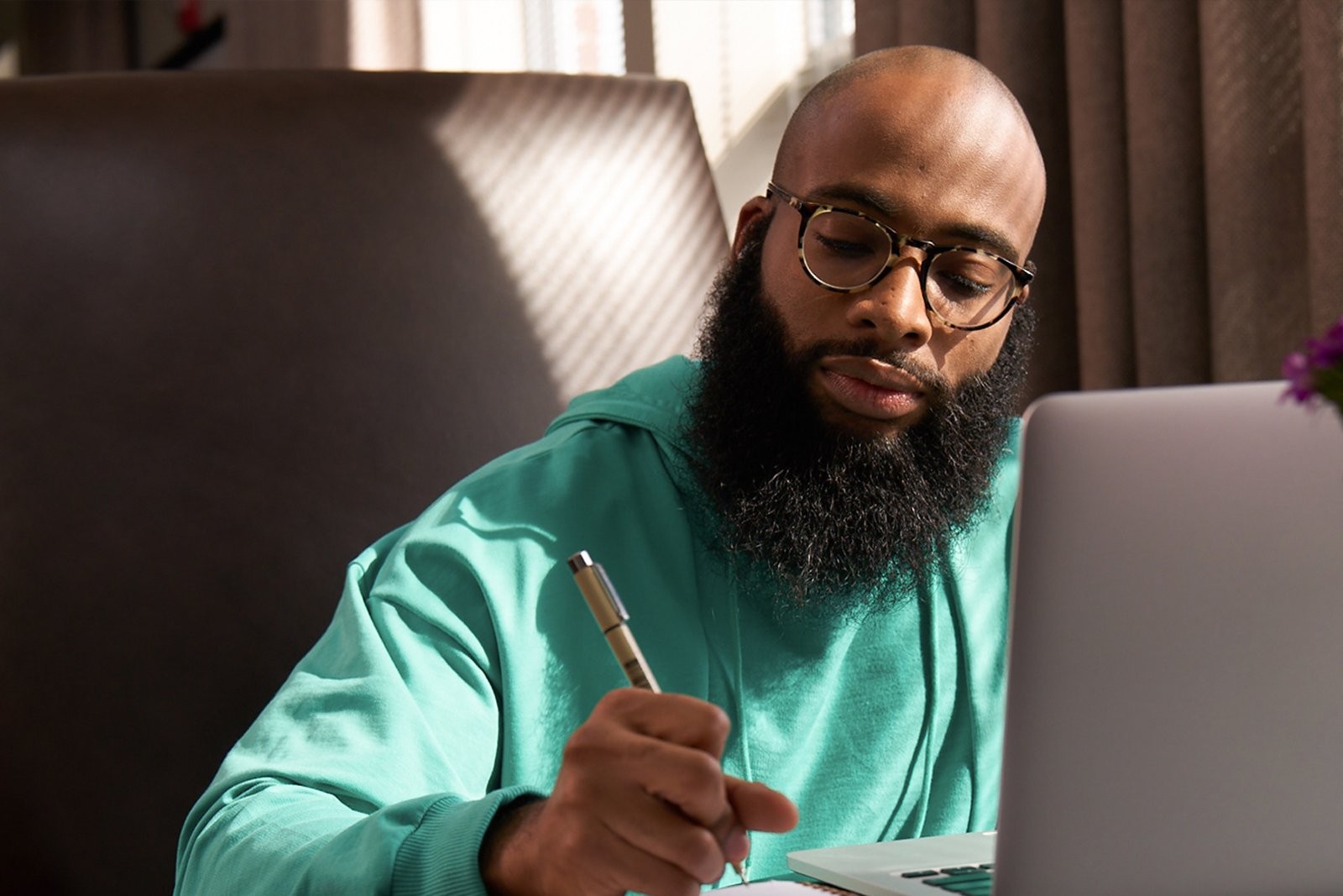 Student working on his laptop writing in a notebook