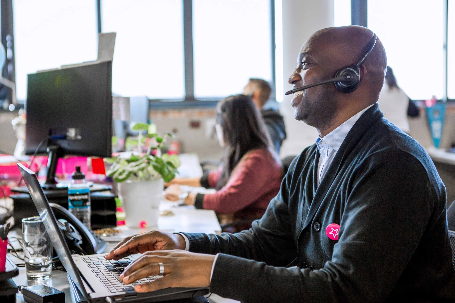 An employee in casual attire works on a laptop at their desk with pink headphones on