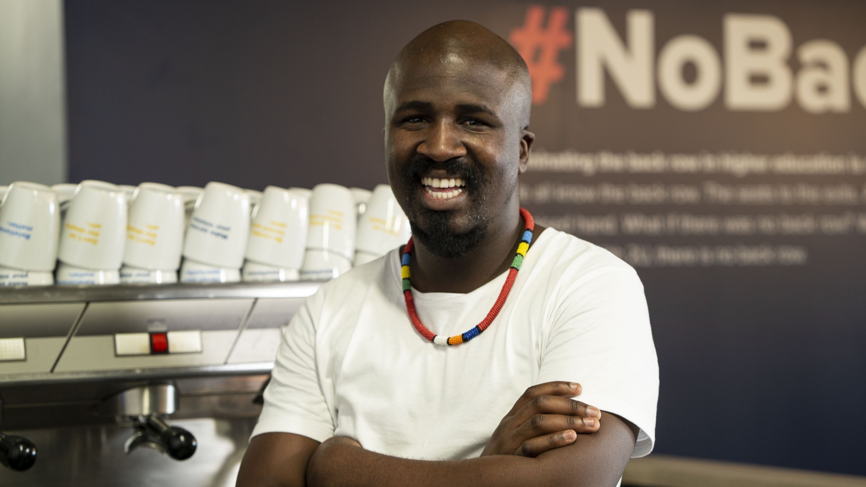 An employee with their arms crossed smiling in front of a coffee machine