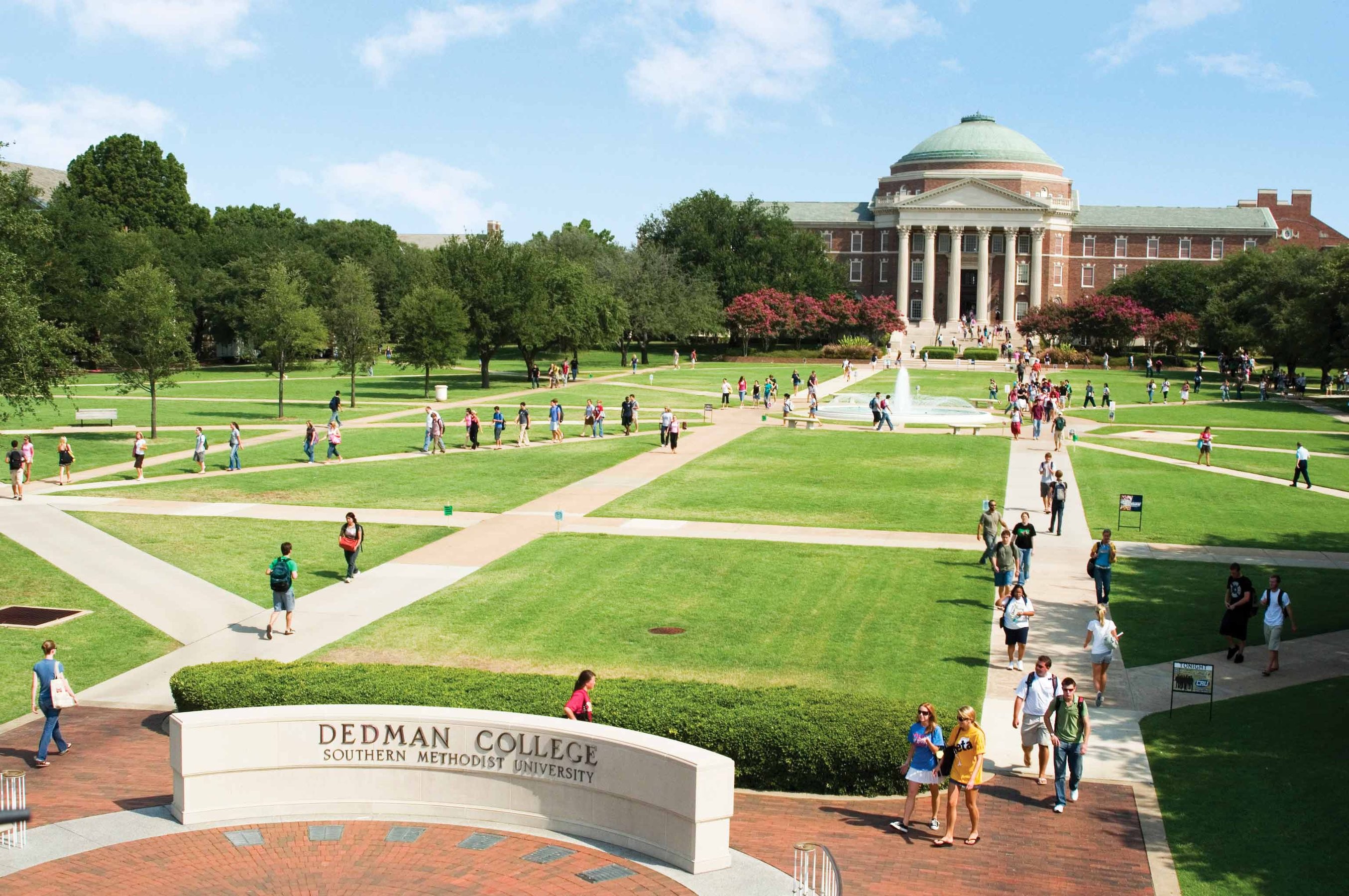 Students walking to class on the quad of Dedman College among Dallas Hall, a fountain, and an Southern Methodist University sign