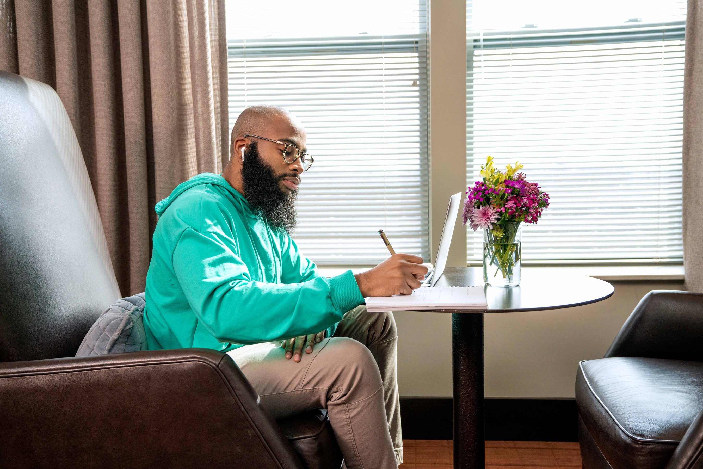 Man wearing a neon colored hooded sweatshirt sitting in a large leather chair and taking notes.