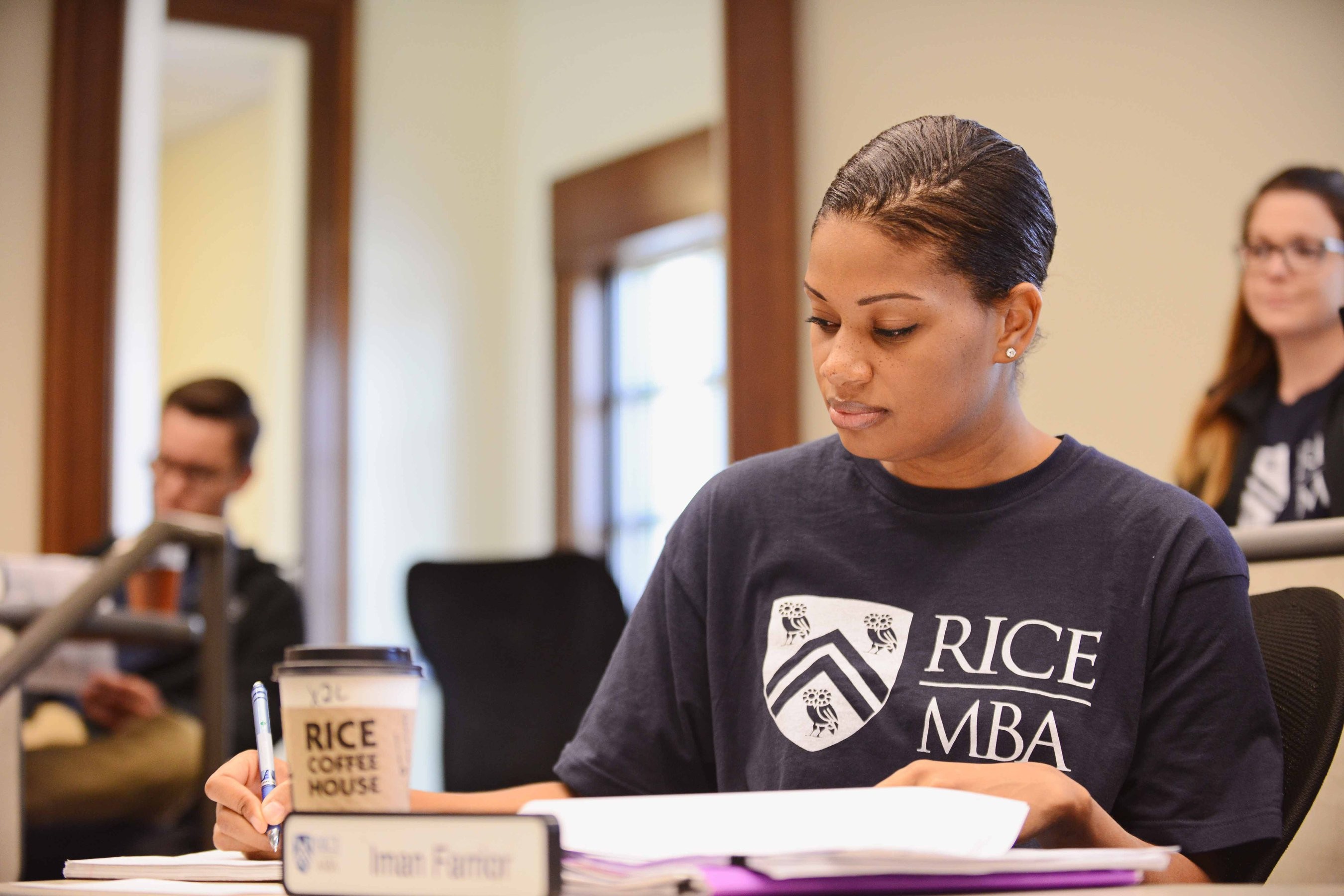 Rice University MBA student taking notes in class with a Rice coffee sleeve on her cup